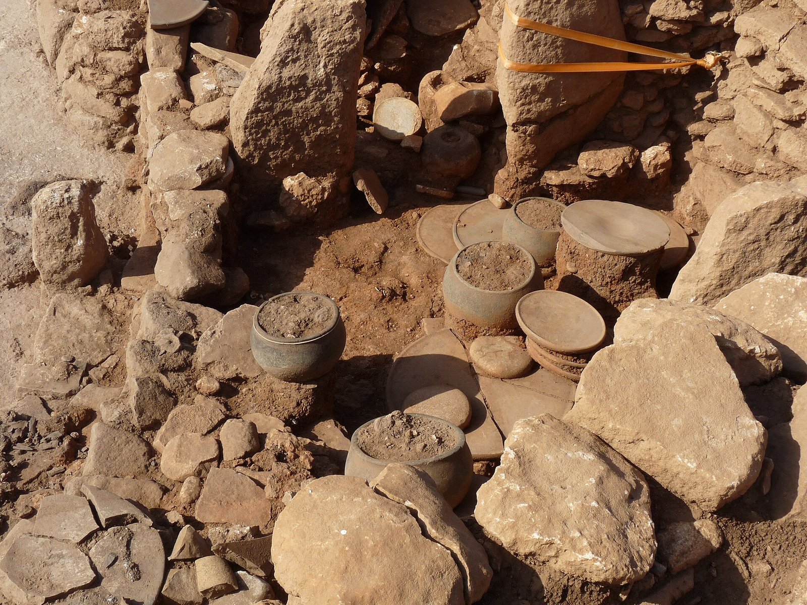In-situ stone vessels at Karahan Tepe. Structure BF yielded stone vessels and plates, three stone rings, and the nested-vessel scene — a smaller vessel set inside a larger one, holding three tiny animal figurines.